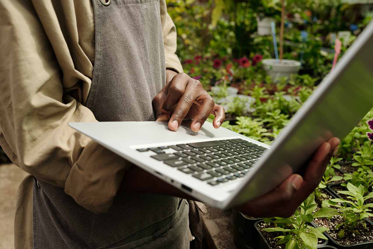 A landscaper using a laptop in a garden setting, managing business and implementing free advertising strategies.