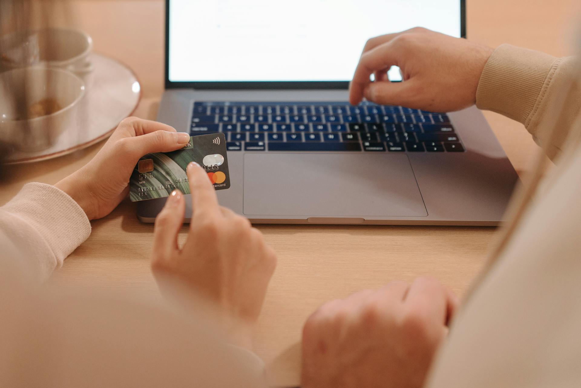 Close-up of hands using a credit card and laptop, showcasing online payment triggered by advertising platforms like Google Ads and Facebook Ads.