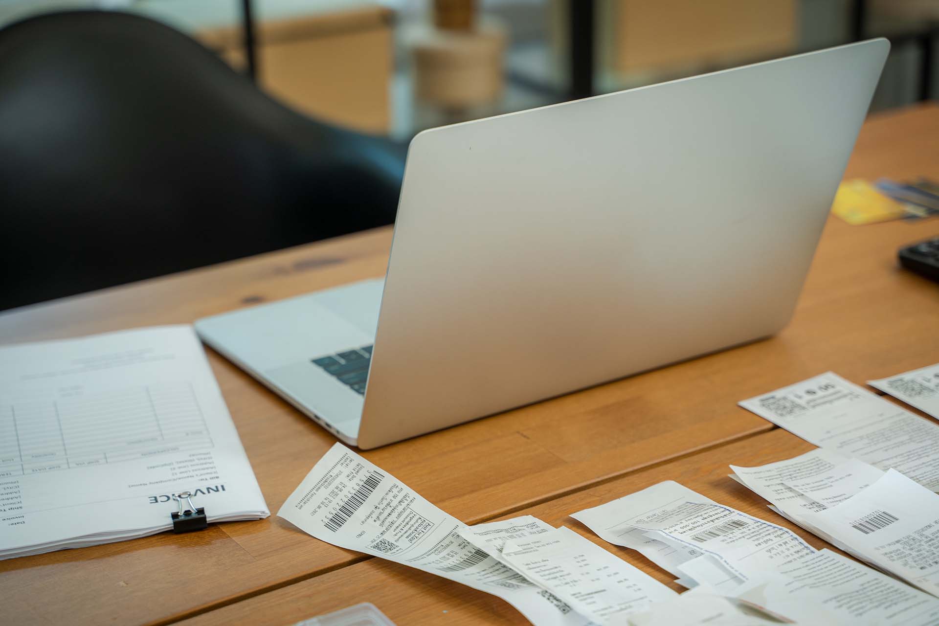 Laptop on a desk surrounded by invoices and receipts, representing financial management features in lawn care software.