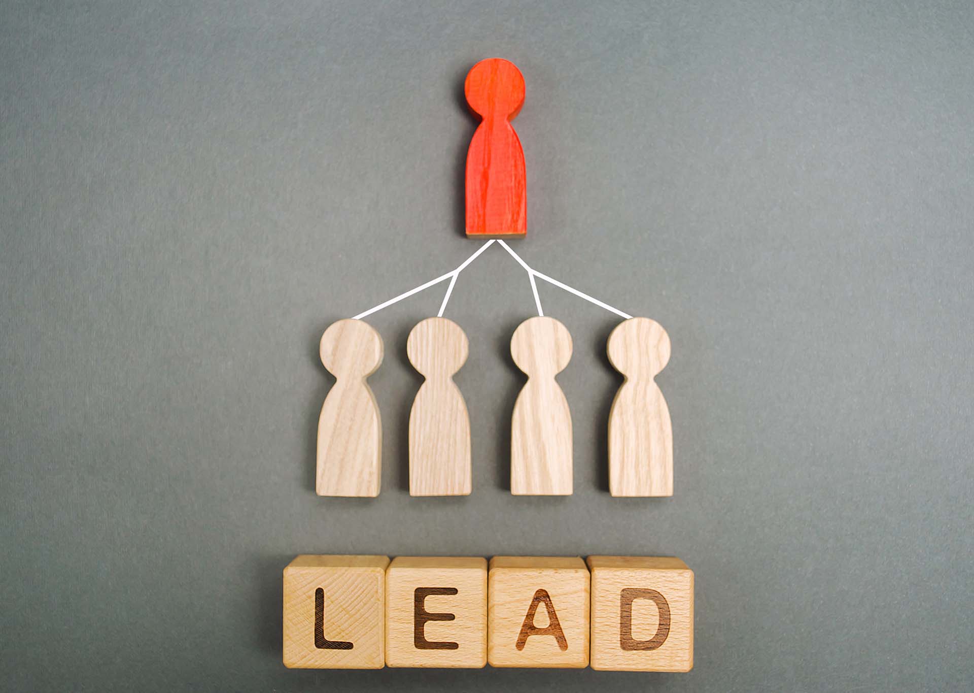 Wooden figurines connected by lines with a red leader figure at the top and blocks spelling 'LEAD' at the bottom, symbolizing leadership and teamwork.