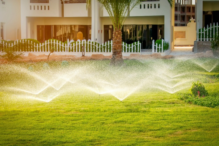 Automated lawn irrigation system watering green grass in front of modern residential building