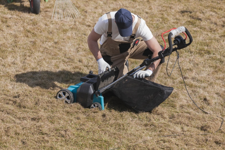 Landscaper cleaning a lawn scarifier during spring yard maintenance on dry grass