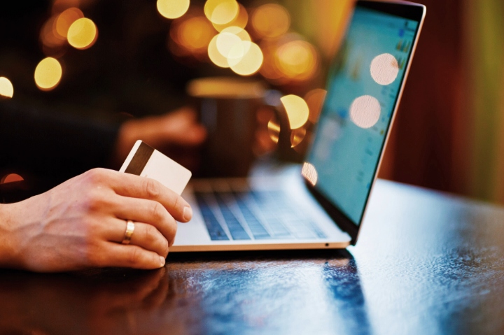 Close-up of a person holding a credit card while using a laptop, representing online payments or digital transactions.