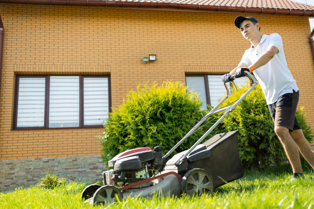 Landscaper mowing a residential lawn in front of a brick house during spring