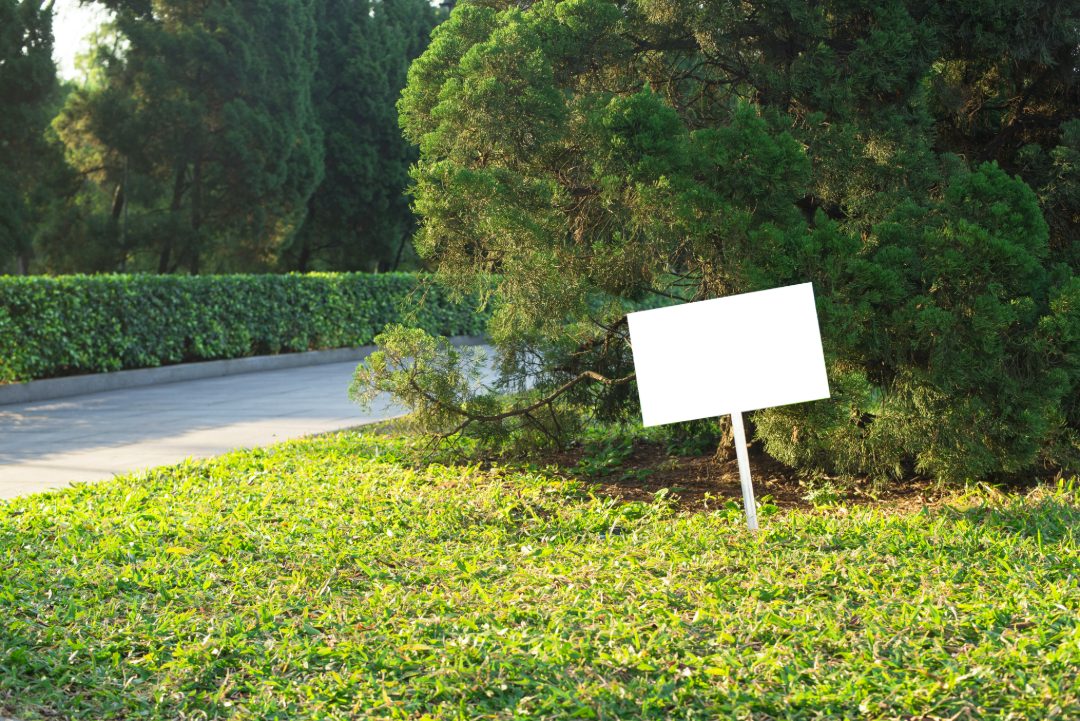 yard sign on a freshly cut lawn near a tree-lined sidewalk, perfect for landscaping or lawn care advertising placement in high-traffic areas