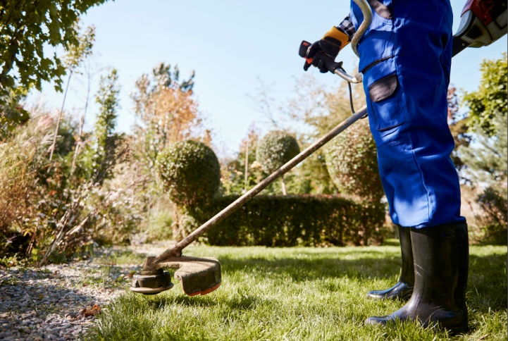 Professional landscaper in blue uniform trimming lawn edges with a string trimmer in a well-kept garden
