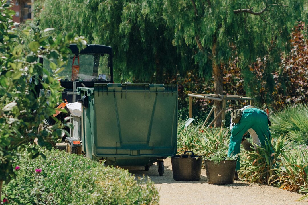 Landscape maintenance worker wearing green overalls tending to plants in a public garden